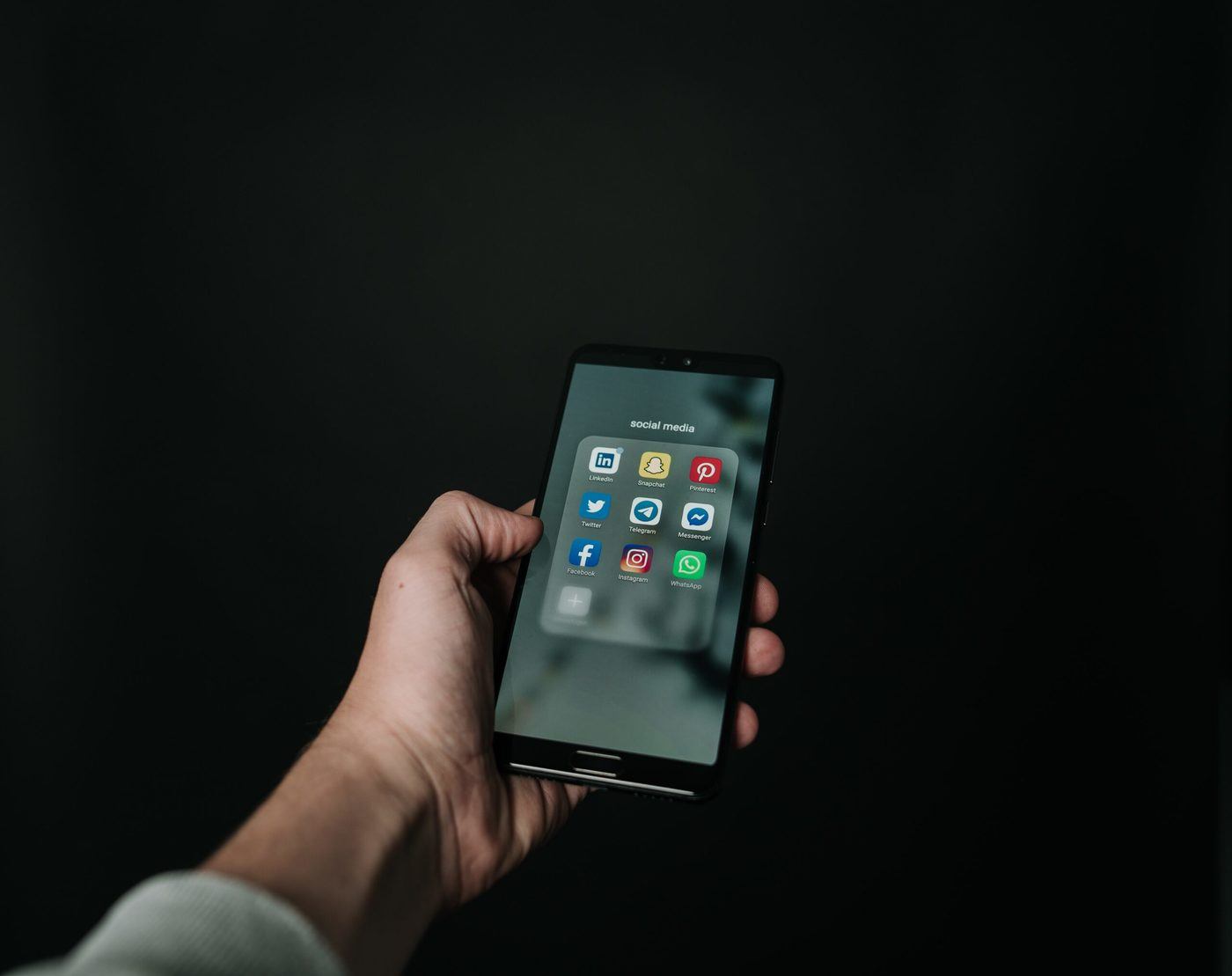 Hand holding a mobile phone with social media icons displayed.