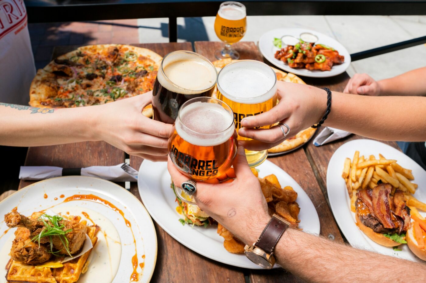 three people cheersing beer glasses in a bear gaden over plates of pizza
